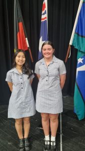 Two students of Nhill College, Charlotte and Messi, pose in front of the Australian, Aboriginal, and Torres Strait flags